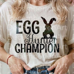 May include: A white t-shirt with black text that reads "Egg Hunter Champion". A black silhouette of a rabbit is next to the text.