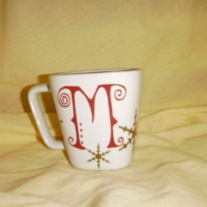May include: White ceramic mug with a red letter "M" and gold snowflake designs.