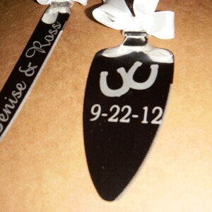May include: A pair of silver cake knives with black handles. One knife is engraved with the text "Denise & Ross" and the other knife is engraved with two horseshoes and the date "9-22-12".