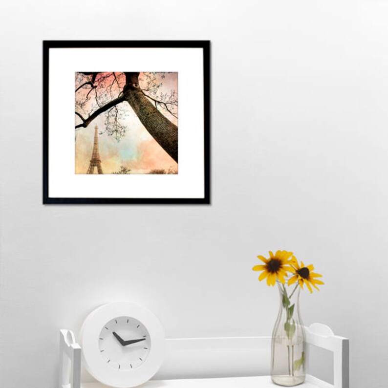 May include: A framed photograph of the Eiffel Tower in Paris, France. The tower is seen through the branches of a tree with a pink and blue sky in the background.