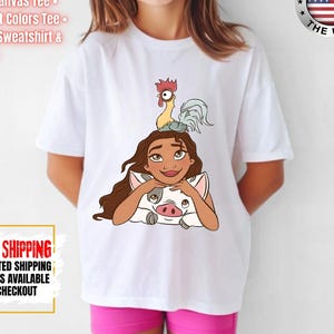 May include: White t-shirt featuring a cartoon illustration of a woman with long brown hair, a pig, and a rooster. The shirt has the text "BELLA-CANVAS 3001Y WHITE" and "FAST SHIPPING". The shirt is made in the USA.