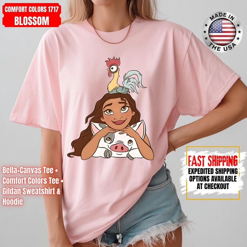 May include: A light pink t-shirt featuring a cartoon illustration of a woman with long brown hair, a pig, and a rooster. The shirt has the text "COMFORT COLORS 1717 BLOSSOM" and "MADE IN THE USA". The shirt is a Bella+Canvas Tee, Comfort Colors Tee, or Gildan Sweatshirt & Hoodie.