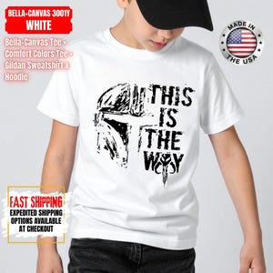 May include: White t-shirt featuring a black graphic of a helmet and the text "THIS IS THE WAY". The shirt is made of a soft material. The image also includes text that says "MADE IN THE USA".