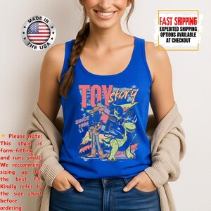 Op de afbeelding: Een blauwe tanktop met de woorden "Toy Story" in roze en geel, met karakterafbeeldingen. De tanktop heeft een ronde halslijn. De tekst "Since 1995" is ook zichtbaar. Gemaakt in de VS.
