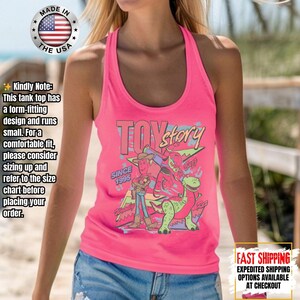 Op de afbeelding: Een felroze tanktop met een Toy Story-afbeelding, inclusief personages en de tekst "Toy Story" en "Since 1995". De tanktop heeft een racerback-ontwerp. De afbeelding bevat ook een "Made in the USA"-logo.