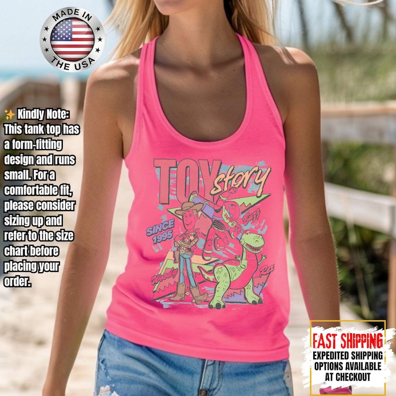 Op de afbeelding: Een felroze tanktop met een Toy Story-afbeelding, inclusief personages en de tekst "Toy Story" en "Since 1995". De tanktop heeft een racerback-ontwerp. De afbeelding bevat ook een "Made in the USA"-logo.