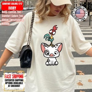 K&ouml;nnte beinhalten: Elfenbeinfarbenes Comfort Colors 1717 T-Shirt mit einem Cartoon-Schwein und Hahn-Design. Das Shirt enth&auml;lt den Text "MADE IN THE USA" und "FAST SHIPPING".