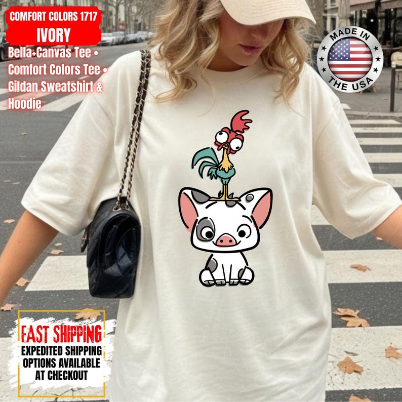 K&ouml;nnte beinhalten: Elfenbeinfarbenes Comfort Colors 1717 T-Shirt mit einem Cartoon-Schwein und Hahn-Design. Das Shirt enth&auml;lt den Text "MADE IN THE USA" und "FAST SHIPPING".