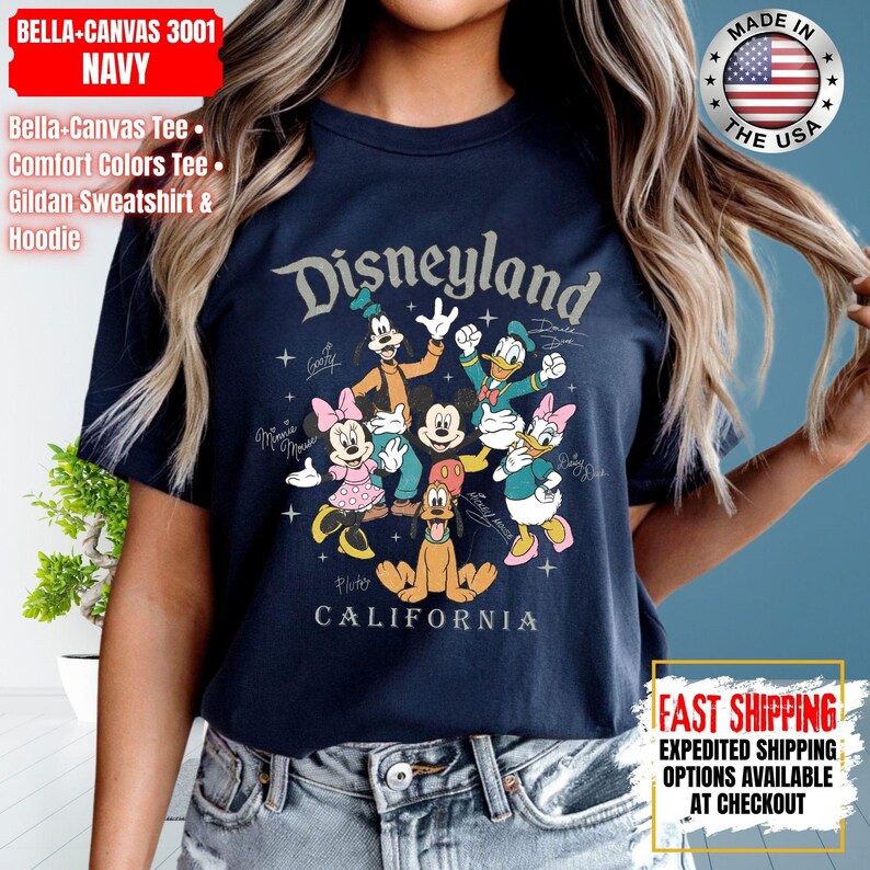 May include: Navy blue t-shirt featuring the word "Disneyland" above a graphic of Disney characters including Mickey Mouse, Minnie Mouse, Donald Duck, and Pluto. The shirt also has the text "CALIFORNIA" below the graphic.