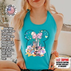 May include: Turquoise tank top featuring a Mickey Mouse silhouette design with a castle, characters, and a pink bow. The shirt has the text "MADE IN THE USA" and "FAST SHIPPING" on it. The tank top has a form-fitting design.