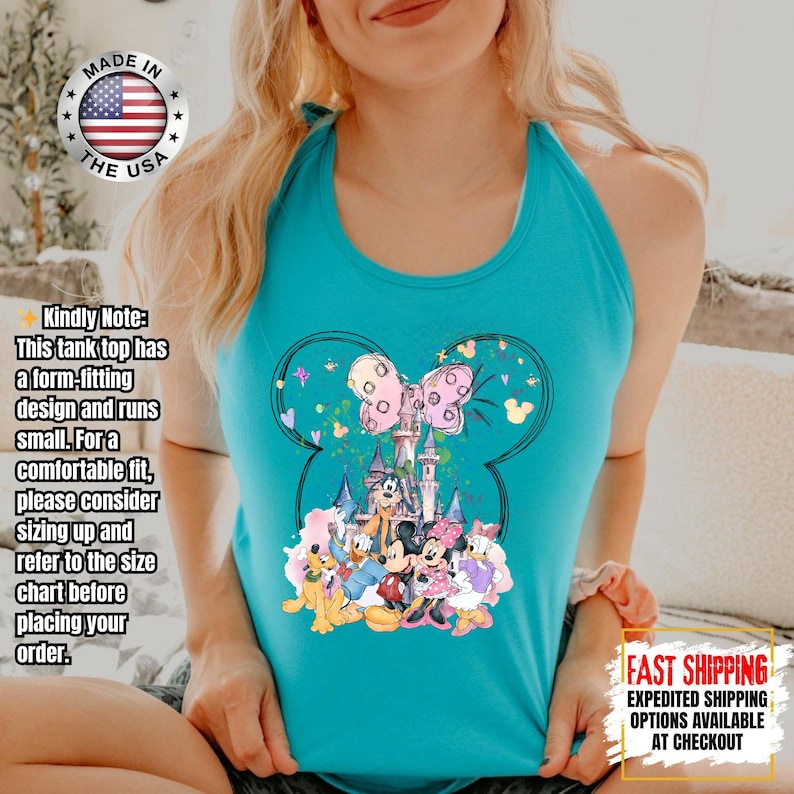 May include: Turquoise tank top featuring a Mickey Mouse silhouette design with a castle, characters, and a pink bow. The shirt has the text "MADE IN THE USA" and "FAST SHIPPING" on it. The tank top has a form-fitting design.