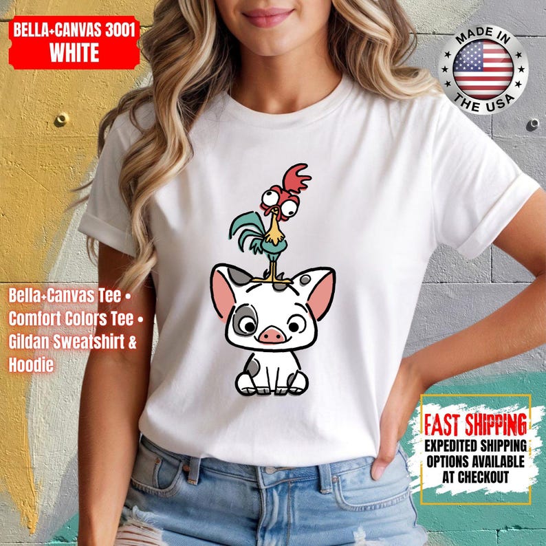 K&ouml;nnte beinhalten: Wei&szlig;es Bella+Canvas 3001 T-Shirt mit einem Cartoon-Schwein und Hahn-Design. Das Schwein ist wei&szlig; mit schwarzen Flecken und rosa Ohren, und der Hahn ist gr&uuml;n, rot und gelb. Das Shirt hat auch den Text "MADE IN THE USA".