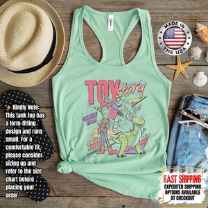 Op de afbeelding: Lichtgroene tanktop met een afbeelding van Toy Story-personages, waaronder Woody, Buzz Lightyear en Rex. De tekst "TOY Story" en "SINCE 1995" zijn ook afgebeeld. Gemaakt in de VS.