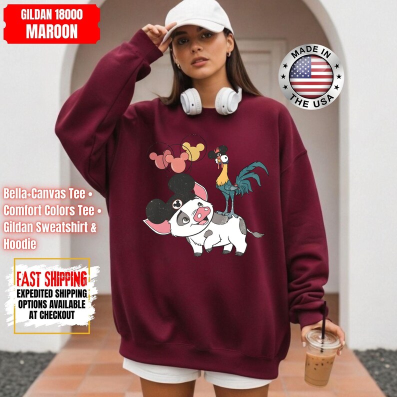 May include: Maroon Gildan sweatshirt featuring a cartoon illustration of a pig with Mickey Mouse ears, a rooster, and Mickey Mouse-shaped balloons. The text "MADE IN THE USA" is on the right. The sweatshirt also has the text "Bella+Canvas Tee", "Comfort Colors Tee", and "Gildan Sweatshirt & Hoodie".