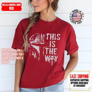 May include: Red t-shirt with the phrase "THIS IS THE WAY" in white, along with a white graphic of a helmet. The shirt is a Bella-Canvas 3001, and the image includes a "Made in the USA" emblem.