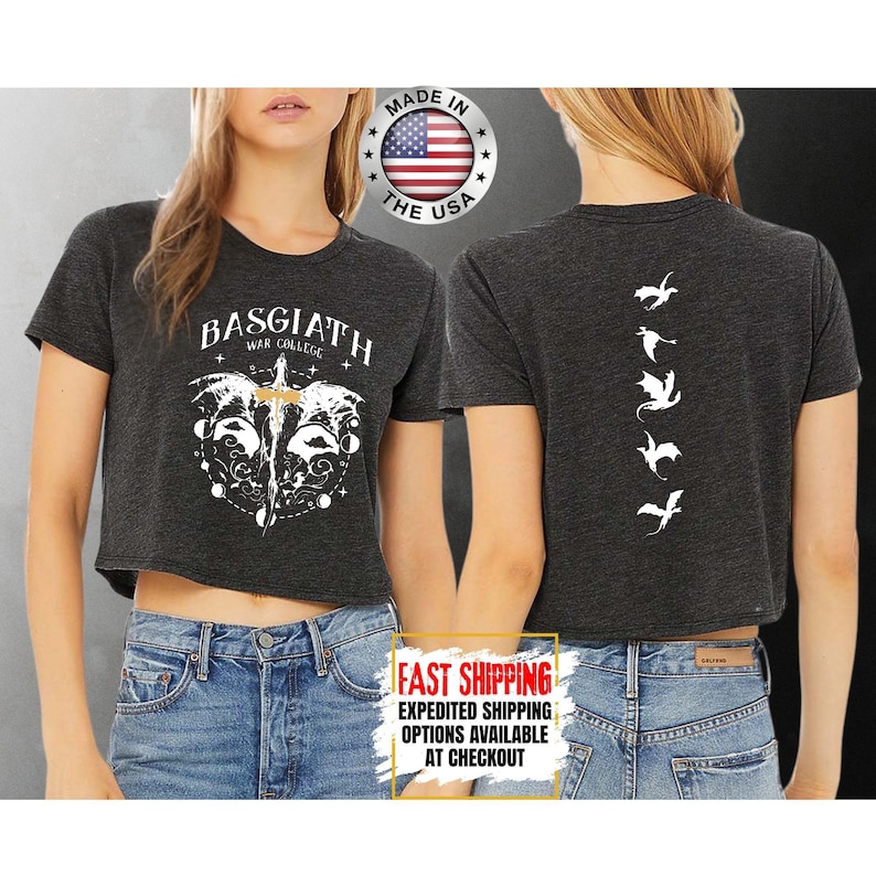 Puede incluir: Top corto gris oscuro con dise&ntilde;os gr&aacute;ficos blancos. La parte delantera muestra "BASGIATH WAR COLLEGE" con un dise&ntilde;o de espada y alas. La parte trasera tiene siluetas de dragones blancos. Hecho en los EE. UU.