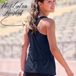 May include: Navy blue racerback vest. The vest is sleeveless with a scoop neck and a racerback design. The text "Next Level 1533 Racerback" is in the upper left corner. The background is a blurred outdoor setting.