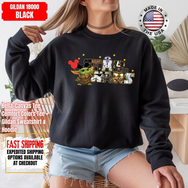 May include: Black sweatshirt featuring a Star Wars graphic with Baby Yoda wearing Mickey Mouse ears. The design includes R2-D2, C-3PO, and other characters. The sweatshirt is a Gildan 18000, and the text "MADE IN THE USA" is visible.