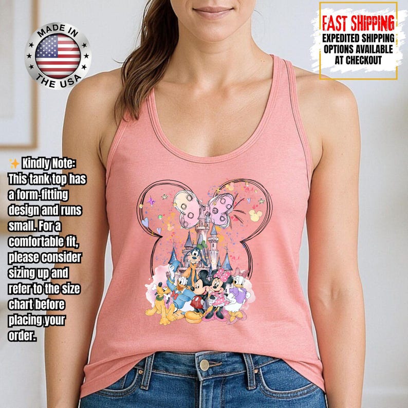 May include: A light pink tank top featuring a Minnie Mouse design. The design includes a castle, a bow, and several cartoon characters. The tank top has the text "MADE IN THE USA".