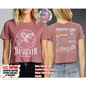 May include: Dusty rose crop top with a white graphic of a dragon inside a circle, the text "BASGIATH WAR COLLEGE" below. The back of the shirt features text and a dragon graphic. Made in the USA.