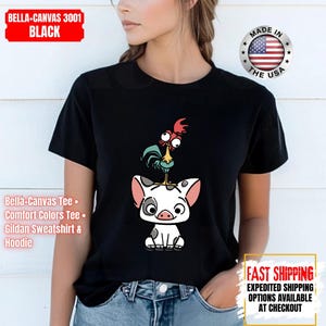 K&ouml;nnte beinhalten: Schwarzes T-Shirt mit einer Cartoon-Illustration eines Schweins und eines Hahns. Das Schwein ist wei&szlig; mit grauen Flecken und rosa Ohren, und der Hahn ist blau, rot und gelb. Das T-Shirt tr&auml;gt den Text "BELLA-CANVAS 3001 BLACK".