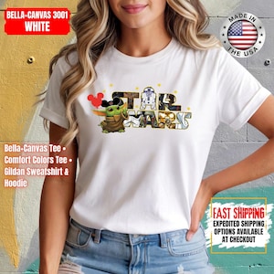 May include: White t-shirt featuring the Star Wars logo with Baby Yoda and Mickey Mouse ears. The shirt includes the text "STAR WARS" and is made of Bella+Canvas 3001 white material. The shirt is made in the USA.