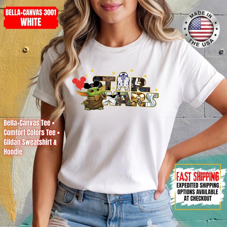May include: White t-shirt featuring the Star Wars logo with Baby Yoda and Mickey Mouse ears. The shirt includes the text "STAR WARS" and is made of Bella+Canvas 3001 white material. The shirt is made in the USA.
