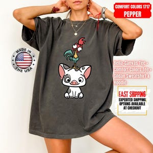 K&ouml;nnte beinhalten: Dunkelgraues Comfort Colors T-Shirt mit einem Cartoon-Schwein und Hahn-Design. Das Shirt enth&auml;lt den Text "MADE IN THE USA" und "COMFORT COLORS 1717 PEPPER". Es ist ein Bella-Canvas Tee, Comfort Colors Tee oder Gildan Sweatshirt & Hoodie.
