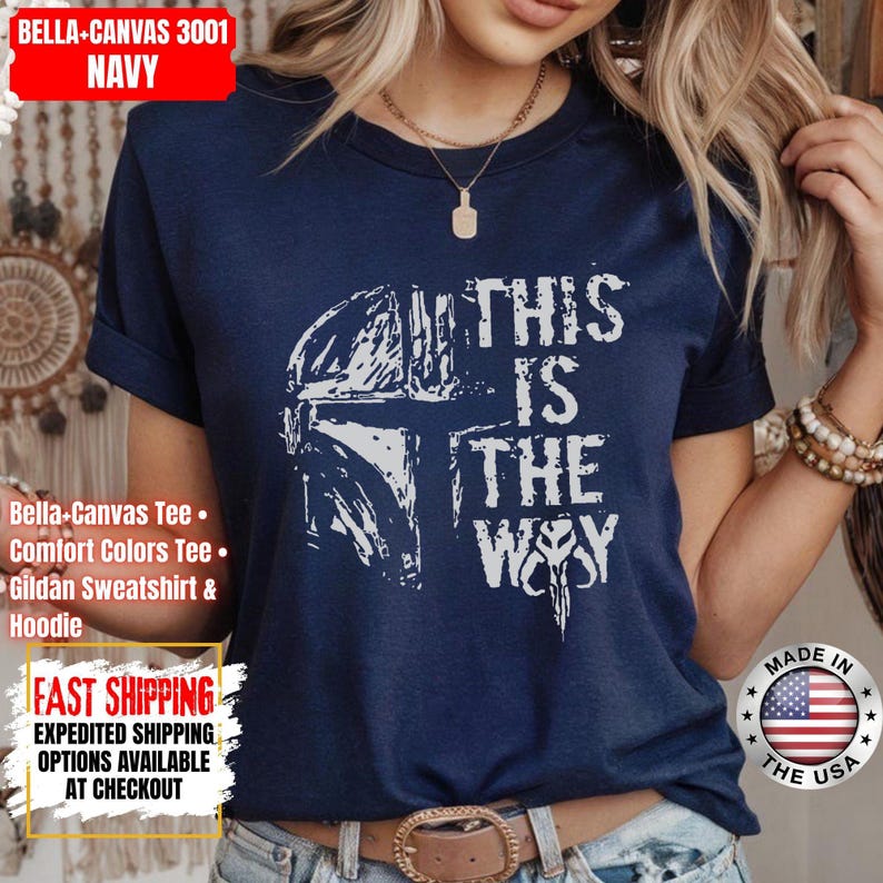 May include: Navy blue t-shirt with a white graphic of a helmet and the text "THIS IS THE WAY". The shirt is made of Bella+Canvas 3001 material. The shirt is a comfort colors tee and Gildan sweatshirt & hoodie.