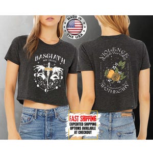Puede incluir: Camisetas cortas de color gris oscuro con dise&ntilde;os gr&aacute;ficos y texto en blanco. Una camiseta presenta "BASGIATH WAR COLLEGE" y un dise&ntilde;o de espada. La otra camiseta tiene "VIOLENCE Basgiath War College" con un dise&ntilde;o naranja y floral. "MADE IN THE USA" est&aacute; impreso en la camiseta.