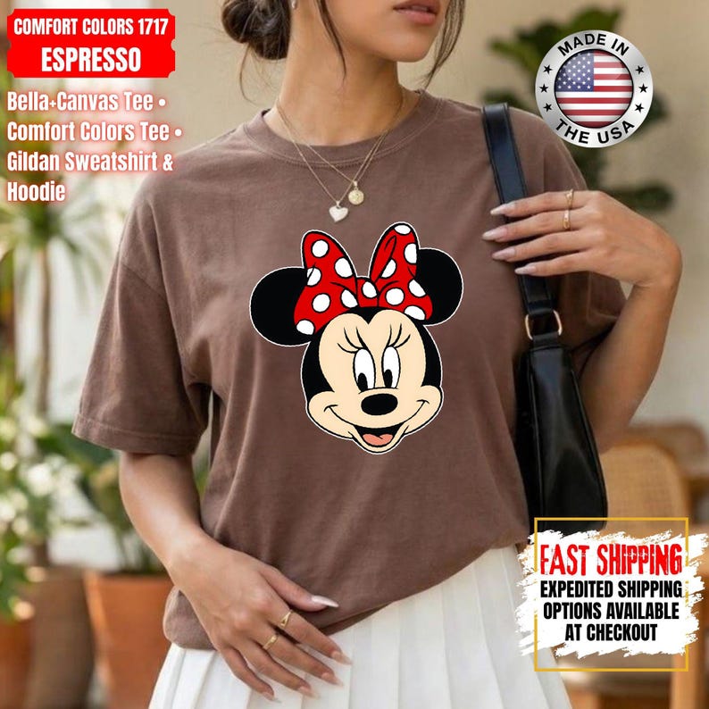 May include: Espresso-colored t-shirt featuring a Minnie Mouse graphic with a red and white polka dot bow. The shirt includes the text "COMFORT COLORS 1717 ESPRESSO" and "MADE IN THE USA". Fast shipping options are available at checkout.