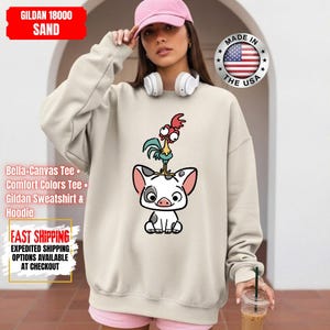 K&ouml;nnte beinhalten: Sandfarbenes Gildan-Sweatshirt mit einem Cartoon-Schwein und einem Hahn-Design. Das Sweatshirt tr&auml;gt den Text "Made in the USA" und "GILDAN 18000 SAND". Das Bild enth&auml;lt auch Text f&uuml;r "Bella-Canvas Tee", "Comfort Colors Tee", "Gildan Sweatshirt & Hoodie" und "FAST SHIPPING".