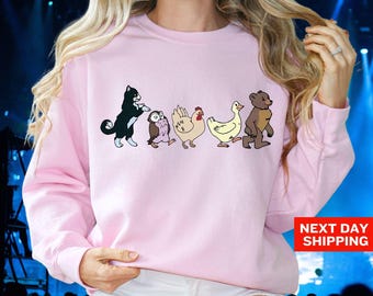May include: Light pink sweatshirt featuring a line of cartoon animals: a black cat, owl, chicken, duck, and bear. The text "LIGHT PINK" is at the top left. The words "NEXT DAY SHIPPING" are at the bottom right.