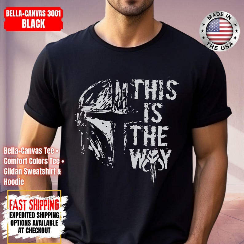 May include: Black t-shirt with a white graphic of a helmet and the text "THIS IS THE WAY". The shirt includes the text "BELLA-CANVAS 3001 BLACK" and "MADE IN THE USA".