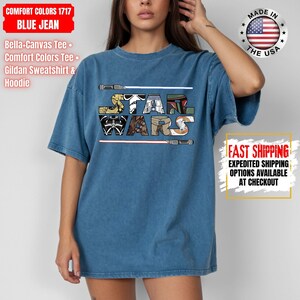 May include: Blue jean Comfort Colors t-shirt with the text "STAR WARS" in a colourful, stylised font. The shirt includes the text "MADE IN THE USA" and "FAST SHIPPING" with expedited options available.