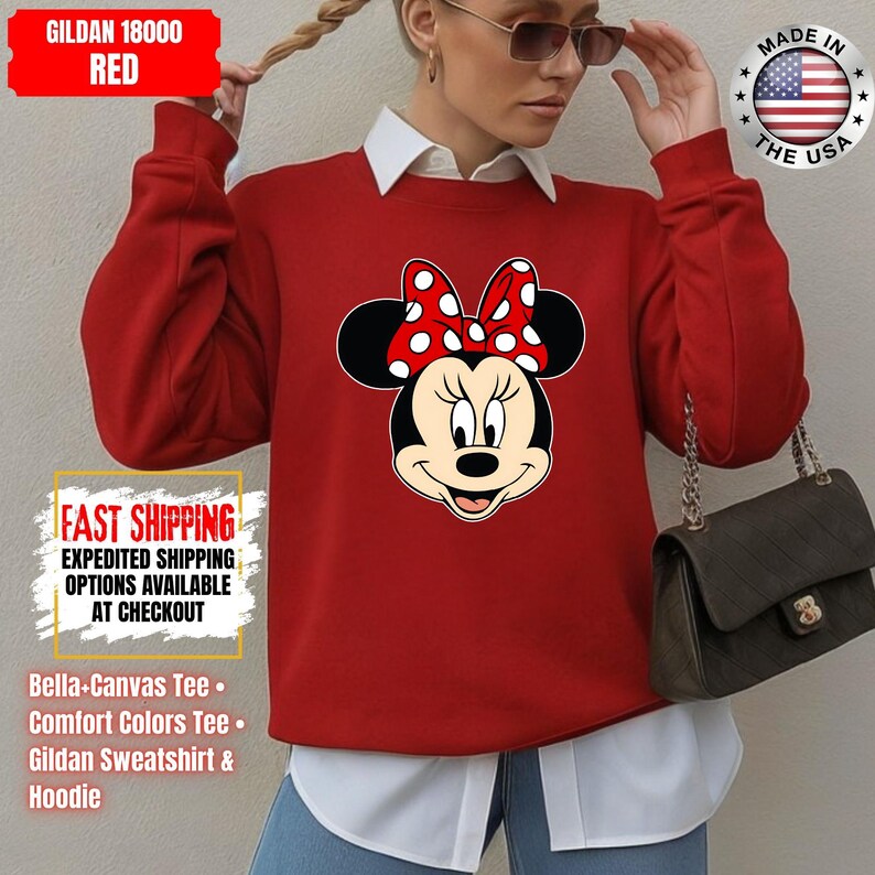 May include: Red Gildan 18000 sweatshirt featuring a Minnie Mouse graphic with a red and white polka dot bow. The sweatshirt has the text "FAST SHIPPING" and "MADE IN THE USA" printed on it. The image also shows a white collared shirt underneath.