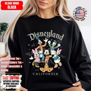 May include: Black Disneyland sweatshirt featuring Mickey Mouse, Minnie Mouse, Donald Duck, Daisy Duck, Goofy, and Pluto. The text "Disneyland" and "California" are printed on the front. Made in the USA.
