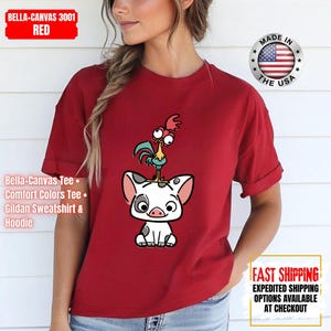 K&ouml;nnte beinhalten: Rotes T-Shirt mit einem Cartoon-Schwein und Hahn-Design. Das T-Shirt hat hochgekrempelte &Auml;rmel. Der Text "Bella-Canvas Tee, Comfort Colors Tee, Gildan Sweatshirt & Hoodie" steht links. Hergestellt in den USA.