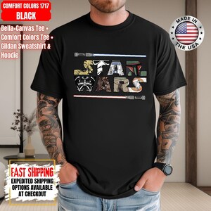 May include: Black t-shirt with the words "STAR WARS" in a colourful, stylised font. The design includes Star Wars imagery, such as lightsabers and character illustrations. Made in the USA.