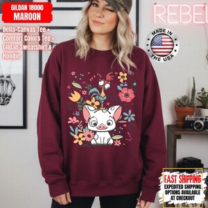 May include: A maroon Gildan sweatshirt with a graphic of a pig, rooster, and flowers. The design includes the text "GILDAN 18000 MAROON". The sweatshirt has a crew neck and long sleeves. Made in the USA.