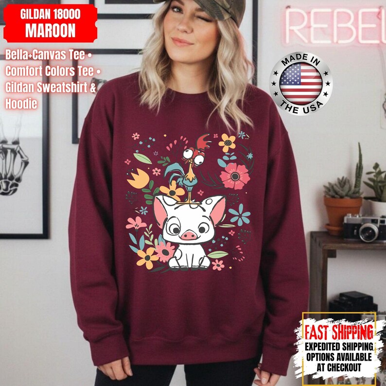 May include: A maroon Gildan sweatshirt with a graphic of a pig, rooster, and flowers. The design includes the text "GILDAN 18000 MAROON". The sweatshirt has a crew neck and long sleeves. Made in the USA.