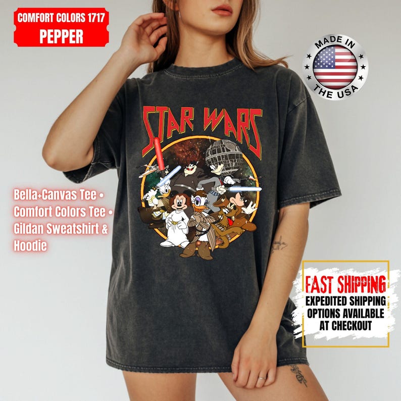 Op de afbeelding: Donkergrijs Comfort Colors T-shirt met een Star Wars-afbeelding met Disney-personages. Het ontwerp bevat de tekst "STAR WARS" in het rood, met een cirkelvormige illustratie van stripfiguren. Gemaakt in de VS.