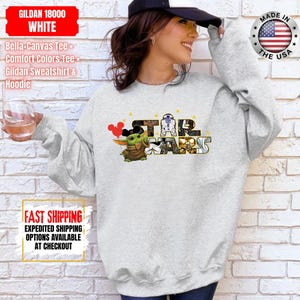 May include: A light gray sweatshirt featuring a Star Wars graphic with Grogu and the text "STAR WARS". The sweatshirt also has the text "GILDAN 18000 WHITE" and "MADE IN THE USA".