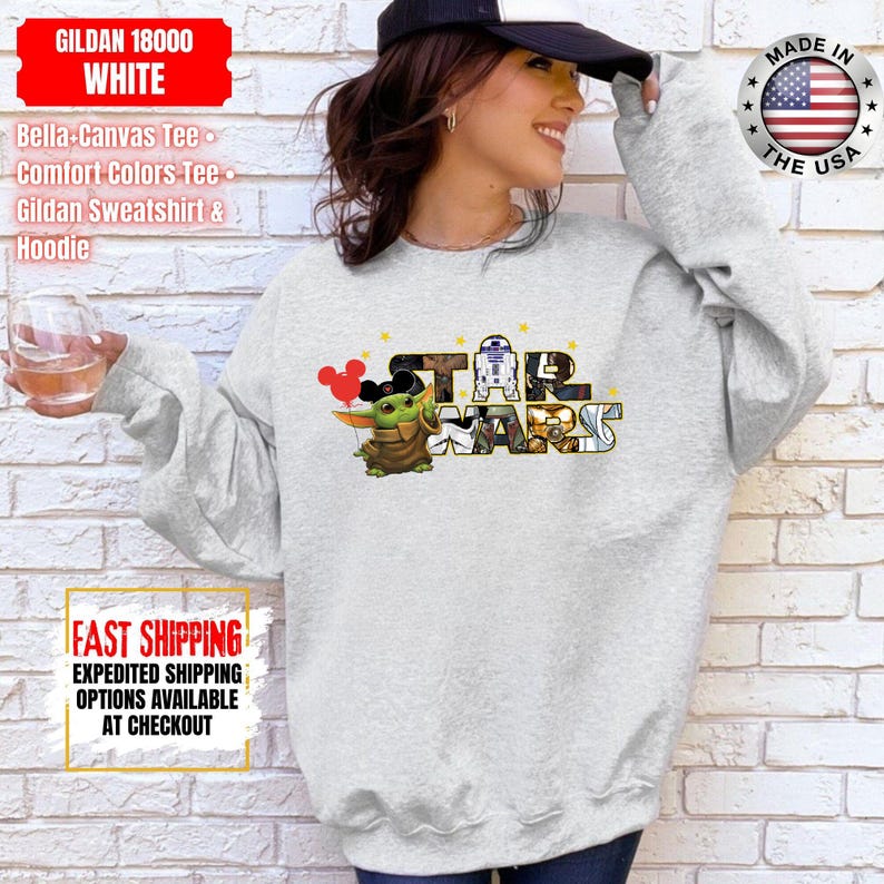 May include: A light gray sweatshirt featuring a Star Wars graphic with Grogu and the text "STAR WARS". The sweatshirt also has the text "GILDAN 18000 WHITE" and "MADE IN THE USA".