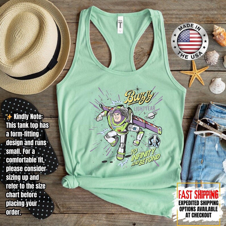 May include: A pale green racerback tank top with a Buzz Lightyear graphic and the phrase "To Infinity and Beyond". The design includes a straw hat, flip-flops, and denim shorts. The tank top is made of a soft material. The image also includes a "Made in the USA" badge.