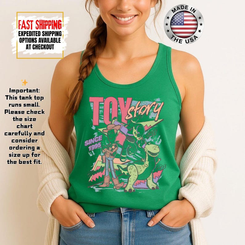 Op de afbeelding: Groen tanktop met roze "TOY Story"-tekst en afbeeldingen van personages uit de film. De tekst "SINCE 1995" is ook zichtbaar. De tanktop heeft een ronde halslijn en is gemaakt in de VS.