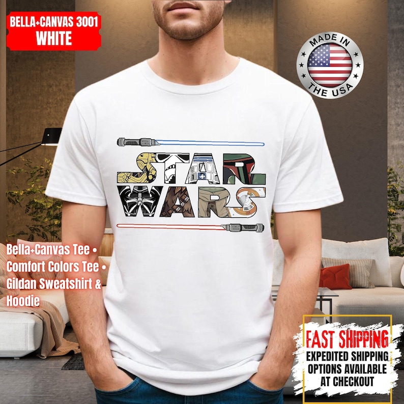 May include: White t-shirt with the words "STAR WARS" in a block-letter design, incorporating Star Wars imagery. Blue and red lightsabers are above and below the text. The shirt is made in the USA.