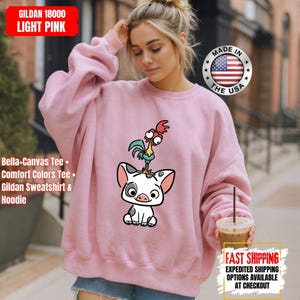 K&ouml;nnte beinhalten: Hellrosa Gildan 18000 Sweatshirt mit einem Cartoon-Schwein- und Hahn-Motiv. Das Sweatshirt tr&auml;gt die Aufschrift "Made in the USA" und "Fast Shipping". Es ist ein Bella+Canvas Tee, Comfort Colors Tee und Gildan Sweatshirt & Hoodie.