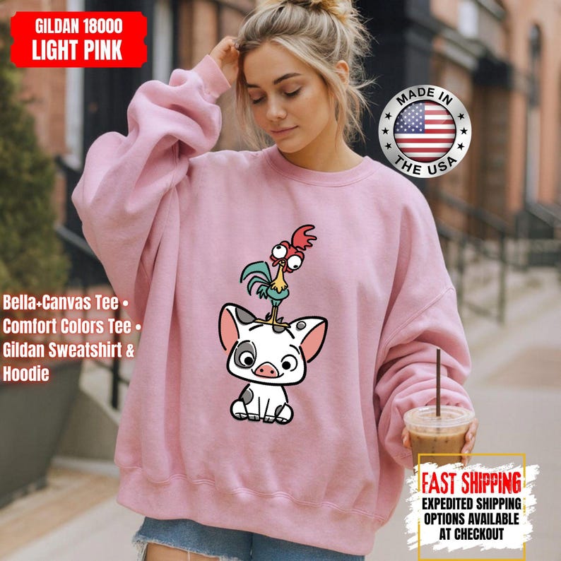 K&ouml;nnte beinhalten: Hellrosa Gildan 18000 Sweatshirt mit einem Cartoon-Schwein- und Hahn-Motiv. Das Sweatshirt tr&auml;gt die Aufschrift "Made in the USA" und "Fast Shipping". Es ist ein Bella+Canvas Tee, Comfort Colors Tee und Gildan Sweatshirt & Hoodie.