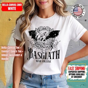 Op de afbeelding: Wit T-shirt met een zwarte afbeelding van een gevleugeld wezen in een decoratief kader, met de tekst "BASGIATH WAR COLLEGE" eronder. Het shirt is gelabeld met "BELLA+CANVAS 3001 WHITE" en "MADE IN THE USA".